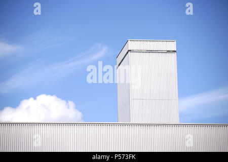 The roof edge of an industrial hall made of corrugated iron in front of a blue sky with clouds. Stock Photo