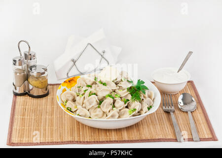 Russian dumplings with herbs and onions. Ravioli with meat. The dish is served in a plate. Served with dumplings is sour cream in a bowl. Stock Photo