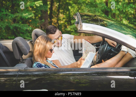 Fashionable young couple sitting in their convertible car and looking at road map. Travel concept. Stock Photo