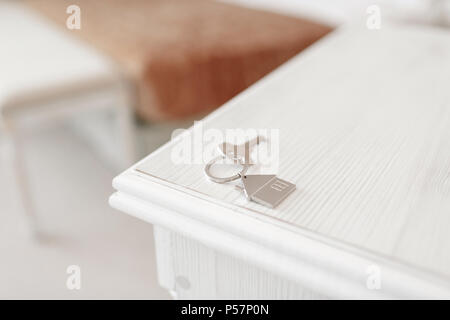Mortgage concept. Key with house keychain on wooden table. Modern light lobby interior. Real estate, moving home or renting property. Stock Photo