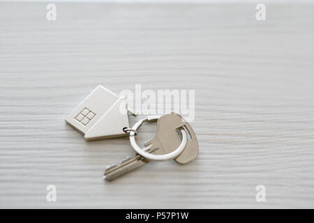 Mortgage concept. Key with house keychain on wooden table. Modern light lobby interior. Real estate, moving home or renting property. Stock Photo