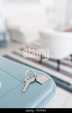 Mortgage concept. Key with house keychain on wooden table. Modern light lobby interior. Real estate, moving home or renting property. Stock Photo