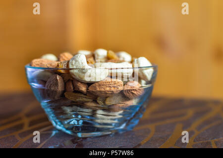 A glass bowl containing mixed dry fruits like almonds, cashew and raisins placed on a table Stock Photo