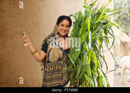 Rural woman holding bunch of crops and sickle Stock Photo