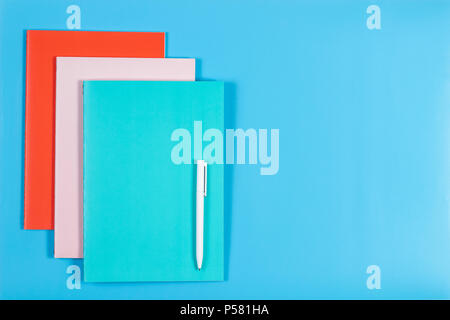 Colorful notebooks and white pen on blue background Stock Photo