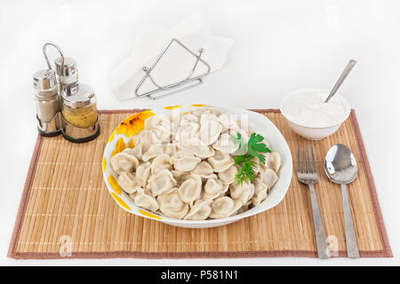 Russian dumplings with herbs and onions. Ravioli with meat. The dish is served in a plate. Served with dumplings is sour cream in a bowl. Stock Photo