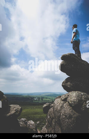 Man standing on a rock looking to the horizon on a cloudy but sunny day at Haytor Rocks in Dartmoor National Park Stock Photo