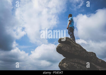 Man standing on a rock looking to the horizon on a cloudy but sunny day at Haytor Rocks in Dartmoor National Park Stock Photo