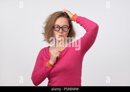 Smart minded woman in funny glasses thinking about excellent idea holding pencil near mouth. Funny teacher thinking about exam or lesson plan. Stock Photo