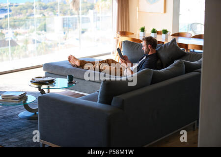 wide image of good looking caucasian man lying on a large couch in a modern living space in a gorgeous house and the latest technologies. Stock Photo