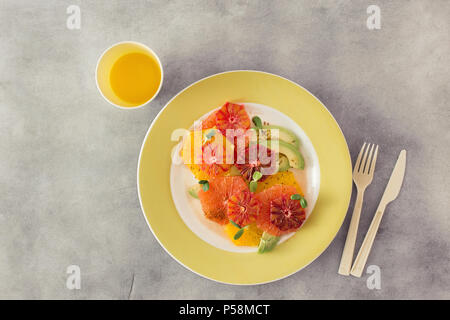 Flat lay healthy and dietary food concept. Healthy summer fruit salad made of oranges, grapefruit and avocado on white concrete background with orange Stock Photo