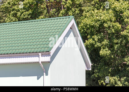 house with green tiled metal roof and white rain gutter on summer trees background Stock Photo