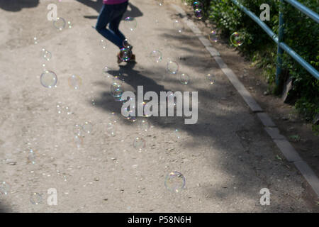 A lot of soap bubbles blower fly down on the asphalt pouring different colors in the sun and in the background play children Stock Photo