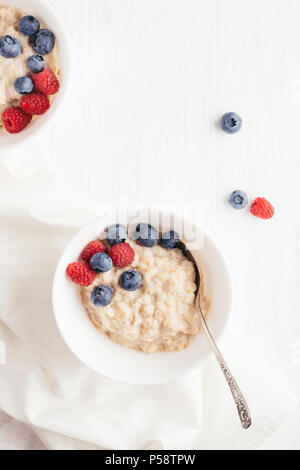 A bowl of oatmeal porridge with blueberries and raspberries on white wooden table. Top view. Stock Photo