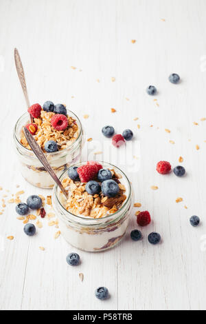 Healthy breakfast. Two jars with tasty parfaits made of granola, berries and yogurt on white wooden table. Shot at angle. Stock Photo