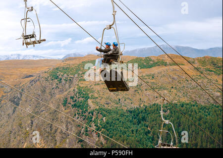 Queenstown, NZ – April 15, 2018: Fun riders with their carts on a cable chair lift going up the hill top for a luge ride with mountains and snow.