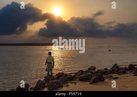 Fisherman watches a fishing boat at sea near Digha rural beach at sunrise. Stock Photo