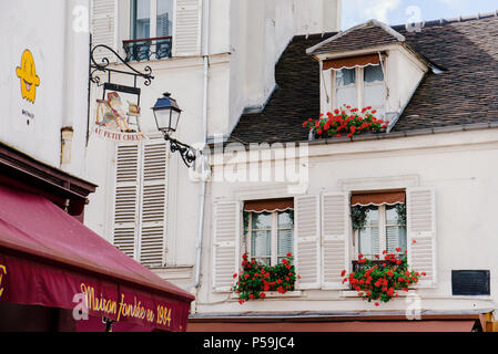 Paris, France - August 10, 2017. Typical Paris mansard windows on white apartment french building with attic, shutters and tile roof with red geranium Stock Photo