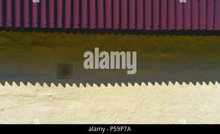 Shadow by the waves from the violet roof shingles on the yellow wall Stock Photo