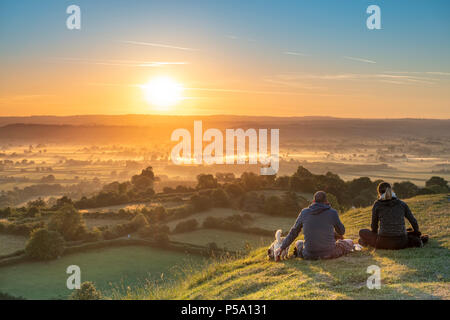 Glastonbury, Somerset, UK. 26th June, 2018. UK Weather - Sitting on top of Glastonbury Tor, a couple and their two dogs watch a beautiful  sunrise over the Somerset Levels, as the West of England is set to see temperatures rise again in to the high twenties. Credit: Terry Mathews/Alamy Live News Stock Photo