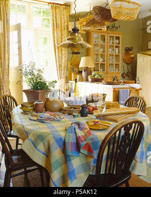 Antique Windsor chairs at table with checked cloth set for breakfast in country kitchen Stock Photo
