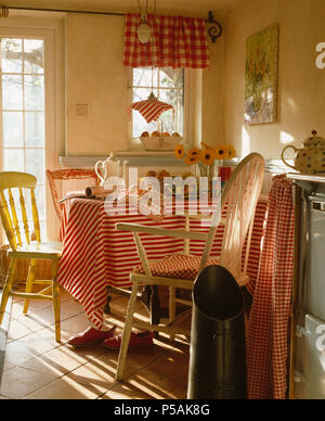Red+white striped cloth on table in cottage kitchen with red+white checked pelmet on small window Stock Photo