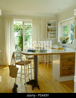 Rush-seated stool at breakfast bar in white country kitchen with French windows and wooden flooring Stock Photo