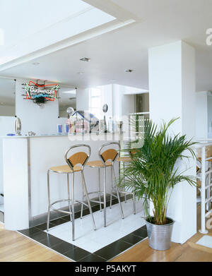 Potted palm in modern open plan kitchen with chrome stools at breakfast bar Stock Photo