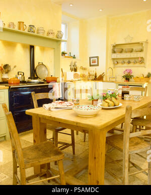 PIne chairs and heavy pine table in yellow country kitchen with black Aga Stock Photo