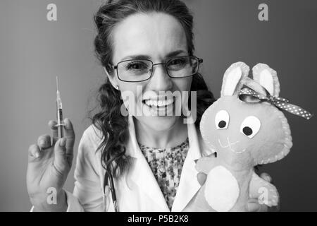 smiling paediatrist doctor in white medical robe with syringe distracting child with toy isolated on background Stock Photo