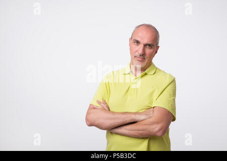 Confident senior man in yellow t-shirt crossing hands on chest and looking at camera Stock Photo