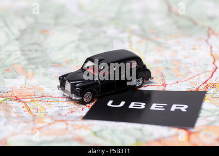 London, UK - MARCH 23rd 2017: A photograph of the Uber logo with a black London style taxi toy car. Uber is a popular taxi style transport service app Stock Photo