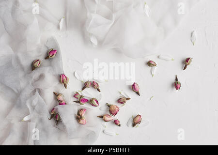 White feminine background with white and gray silk, white petals and dried roses. Copy space, slate background or texture. Concept. Stock Photo