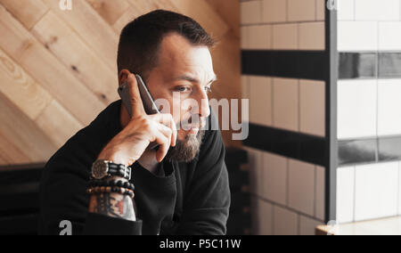 Young tattooed man talking by phone in cafe close up. Stock Photo