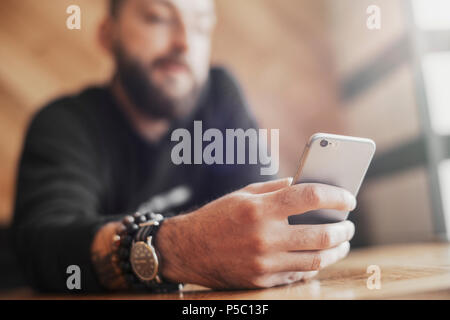 Young tattooed man holding mobile phone in right hand close up. Stock Photo