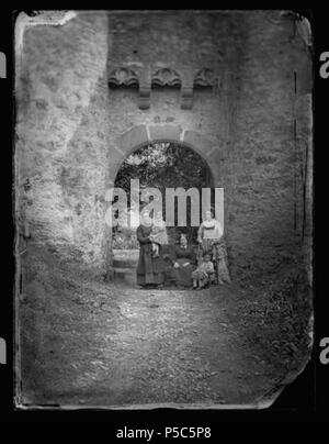 Français : Cornusson. Sous le corps de garde, Caroline, Me Cambe, Paul, Henri .  Français : Château de Cornusson, commune de Caylus (Tarn-et-Garonne). Vers 1870. Photographie de famille sous le corps de garde du château. De gauche à droite, vue de face Henri Trutat (fils d'Eugène) dans les bras d'une femme, Mme Cambe (belle-mère d'Eugène) assise sur une chaise, contre le mur et vue de profil Caroline Cambe (femme d'Eugène) vêtement long, tablier, coiffure ; à ses pieds Paul Trutat (fils d'Eugène) vue de face assis sur une chaise ; en arrière plan végétation. . circa 1870. N/A 381 Cornusson. So Stock Photo