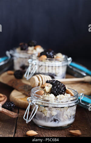 Overnight oatmeal with blackberries, honey and almond milk on a rustic wood background  in a canning glass bail jars with attached lid. Stock Photo