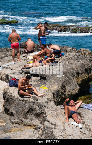 Men sunbathing on rocks at Ras Beirut beside The Corniche in Beirut, Lebanon. Stock Photo