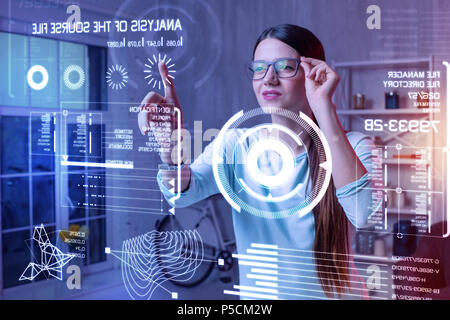Clever woman smiling and touching her glasses while looking at the screen Stock Photo