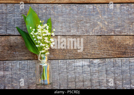 Bouquet of flowers beautiful smell lily of the valley or may-lily in glass vase on rustic old vintage wooden background. Garden in spring or summer co Stock Photo