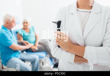 female doctor with her senior patients in the background, focus on foreground, on smiling part of doctor's face. Stock Photo
