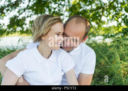 ouple in love. Man and woman in an embrace. A couple sitting in the grass in white T-shirts. Stock Photo