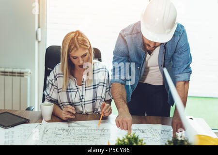 Young worried architect colleagues talking and analyzing blueprints while working on a new project at the office. Stock Photo