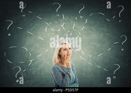 Puzzled young woman in front of a blackboard try to solve different tasks, having a lot of questions. Inspiration concept and self development. Stock Photo