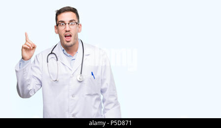 Handsome young doctor man pointing finger up with successful idea. Exited and happy. Number one. Stock Photo