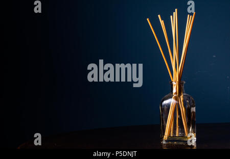 Reed diffusers in a small glass bottle on a table with a navy blue background with copy space on the left Stock Photo