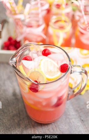 Raspberry lemonade garnished with fresh lemon and raspberries in glass pitcher. Stock Photo