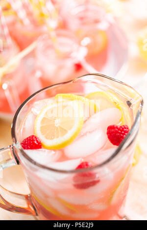 Raspberry lemonade garnished with fresh lemon and raspberries in glass pitcher. Stock Photo
