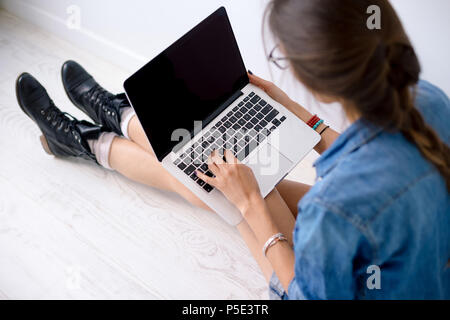Close-up portrait of womans hands working on her laptop keyboard, while sitting on white flor holding the computer on her long legs. Stock Photo