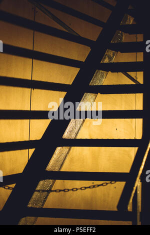 Metal ladder creates long black shadow lines on the wall during sunset Stock Photo